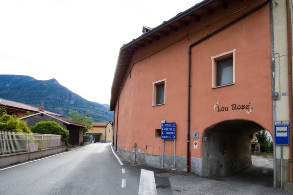 Un bâtiment sur lequel on peut lire l’inscription « Lou Rose », ainsi que des panneaux indicateurs indiquant la direction de Montey, Grand Velt et Pinedo.