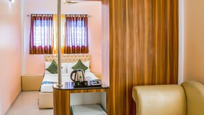 A hotel room with a bed, a bedside table with a kettle, a cup, and a tray with a book and a remote control. - Treebo Naunidh Suites (Pune)
