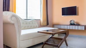 A modern living room with a white sofa, a wooden coffee table, a flat-screen TV mounted on the wall, and a radiator below. - Treebo Naunidh Suites (Pune)