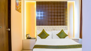 A hotel room with a bed, a nightstand, a wall-mounted artwork, and a patterned curtain. - Treebo Naunidh Suites (Pune)