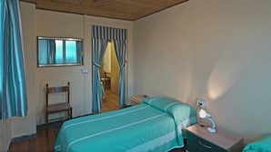 Un dormitorio con techo de madera, una cama con colcha verde, una mesita de noche con lámpara y una silla.