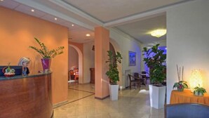 Un hall de hotel con mostrador de recepción, plantas en macetas y una zona de estar.