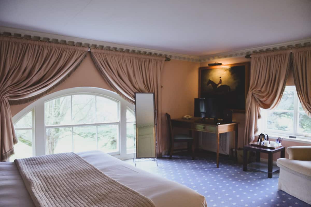 Ein Hotelzimmer mit einem großen Bett, einem Schreibtisch mit Stuhl, einem Fernseher und einem Fenster mit Vorhängen.