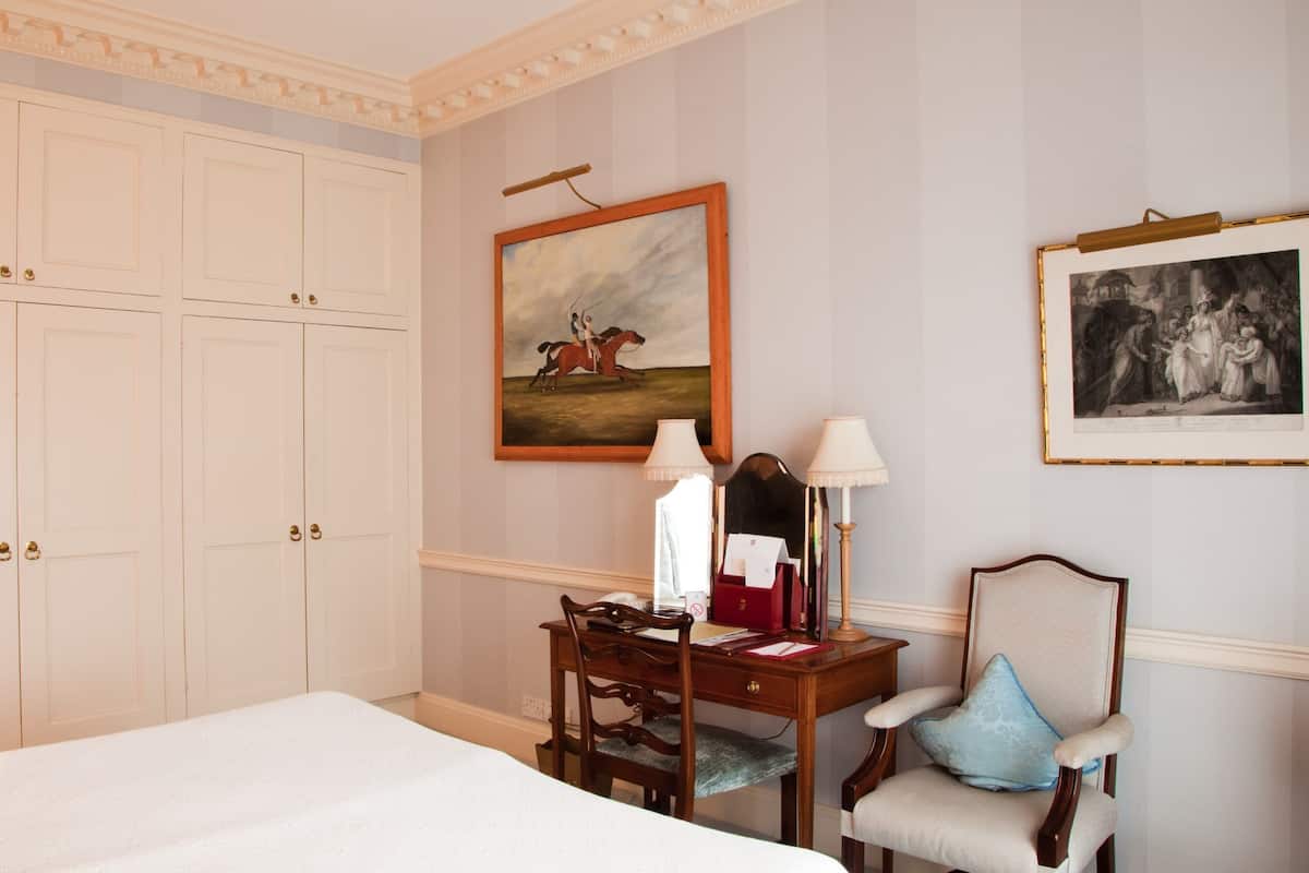Ein Hotelzimmer mit einem großen Bett, einem Schreibtisch mit Lampe, einem Sessel und zwei gerahmten Bildern an der Wand.