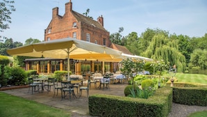 Een gebouw van baksteen met een terras, compleet met tafels en stoelen onder een grote parasol.