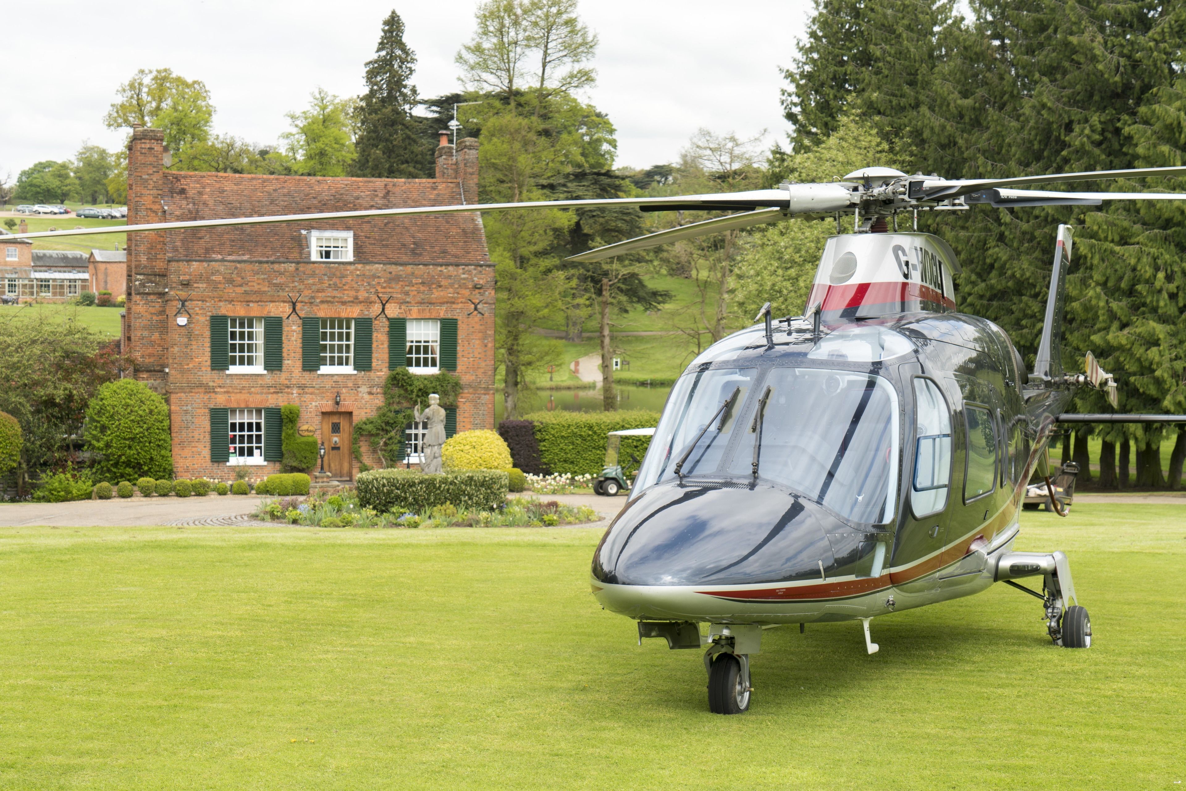 A helicopter parked on a grassy area with a brick building in the background.