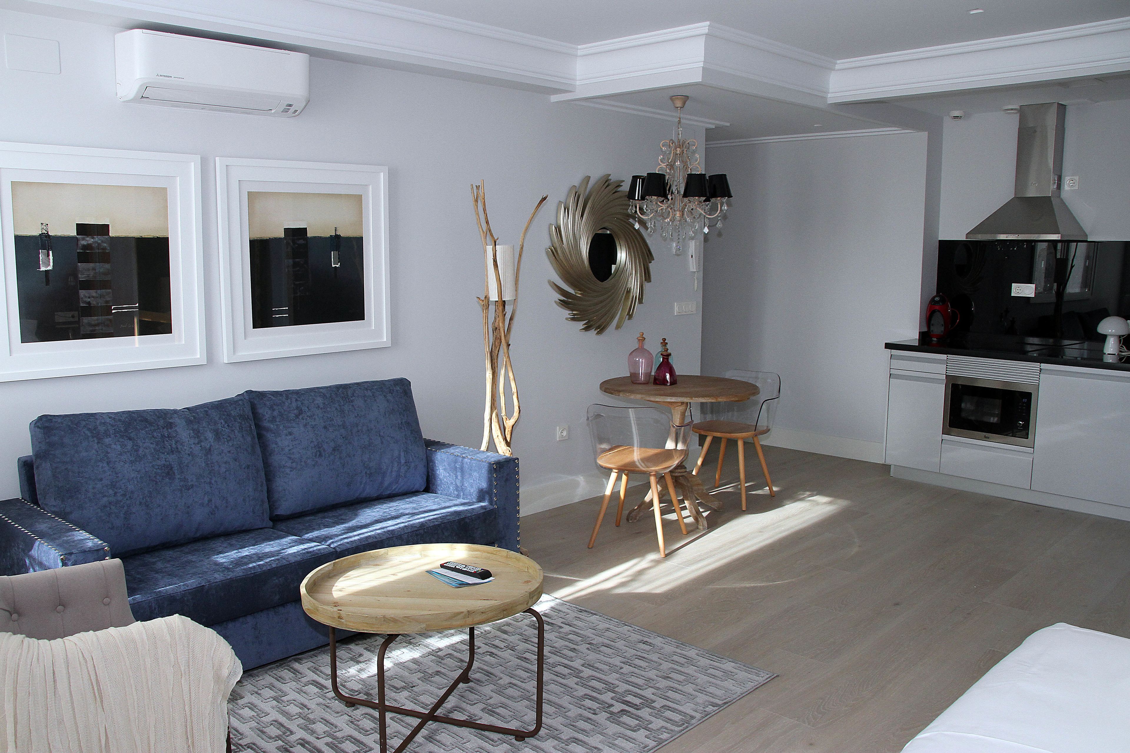 A modern living room with a blue sofa, a wooden coffee table, and a dining area with a chandelier.