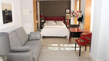 A hotel room with a bed, a grey sofa, a red chair, and a small table with a lamp.