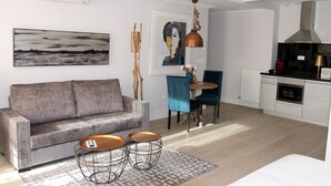 A modern living room with a grey sofa, a coffee table, and a dining area with a blue chair and a table. - Principia Suites (León)