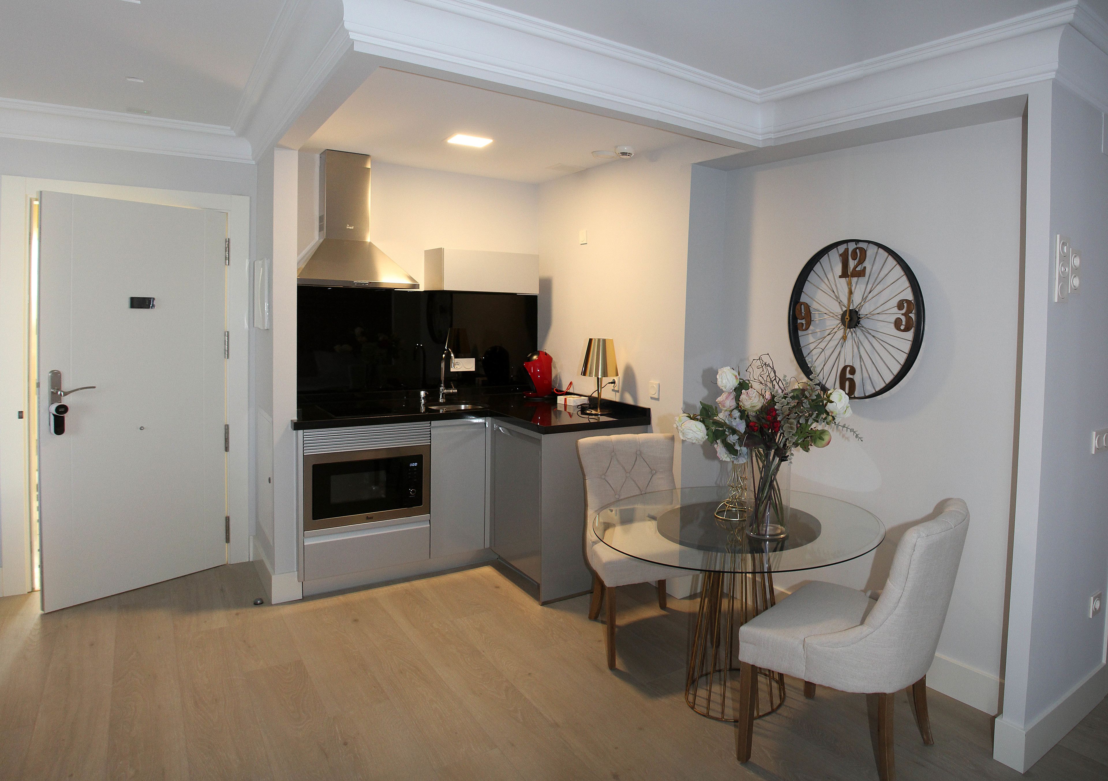 Una cocina moderna con comedor, un reloj en la pared y una puerta que da a otra habitación.