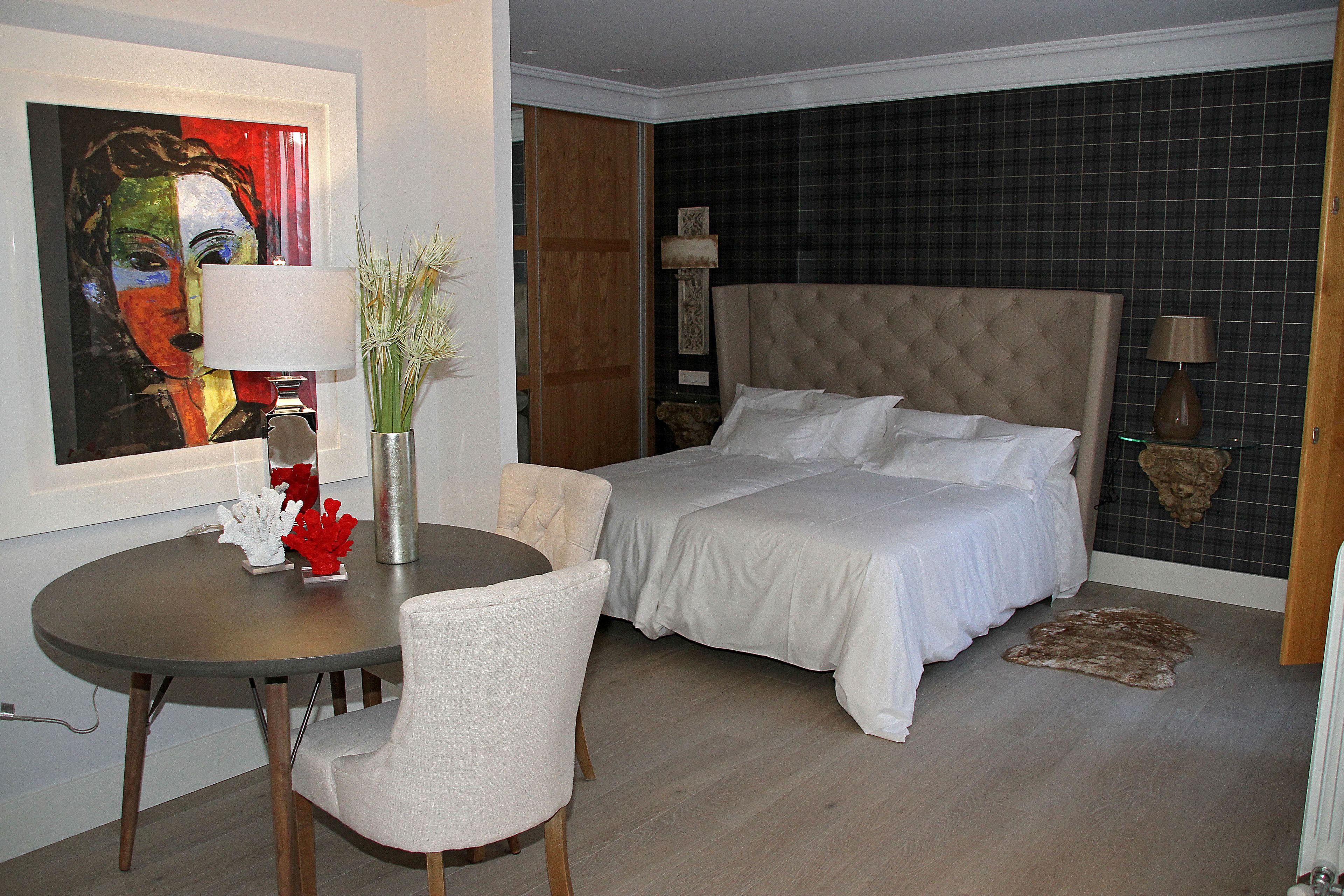 A hotel room with a bed, a desk, a chair, a lamp, a painting, and a rug.