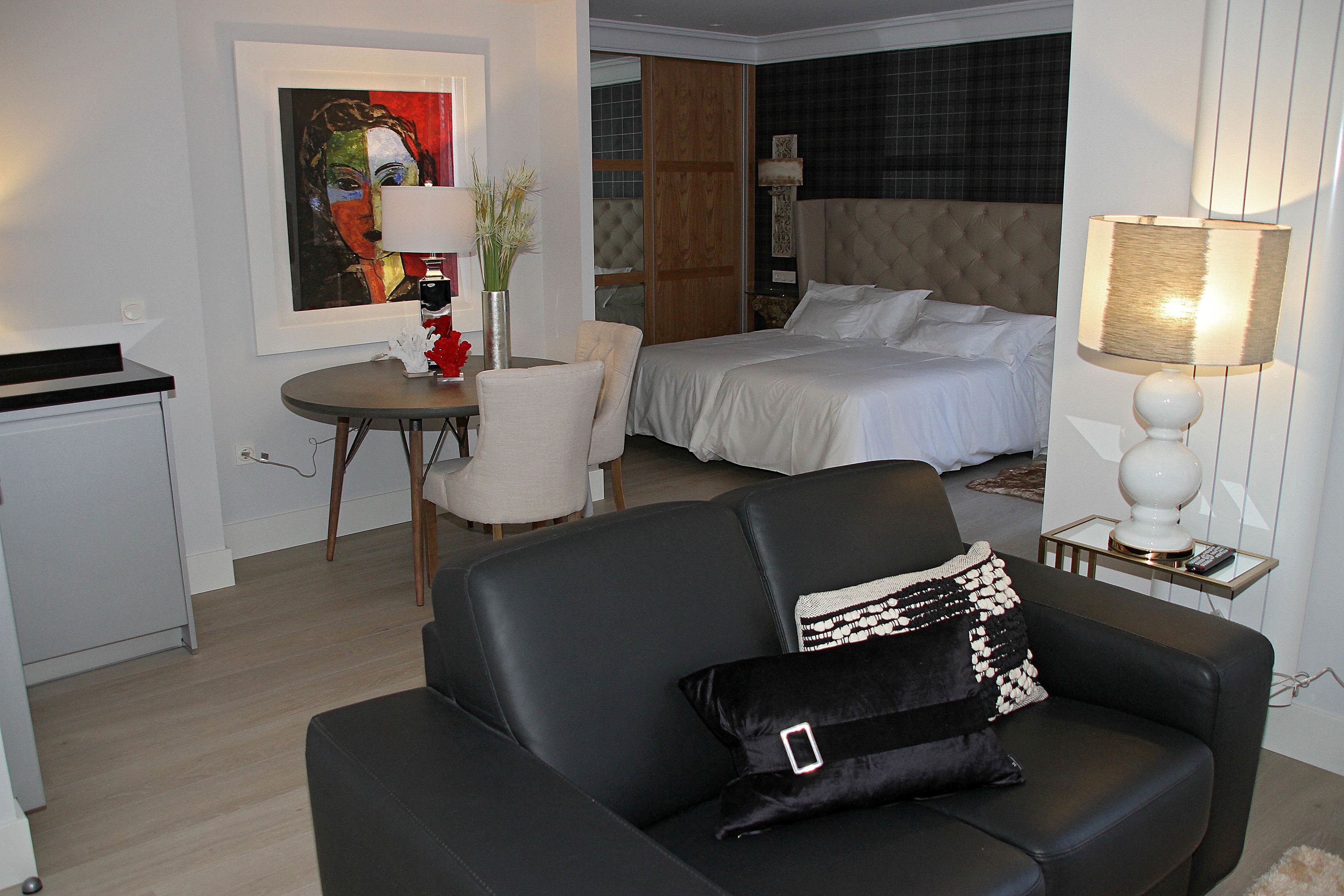 A hotel room with a bed, a sofa, a dining table, and a painting on the wall.