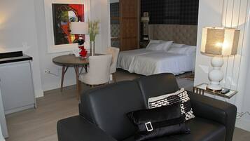 A hotel room with a bed, a sofa, a dining table, and a painting on the wall.
