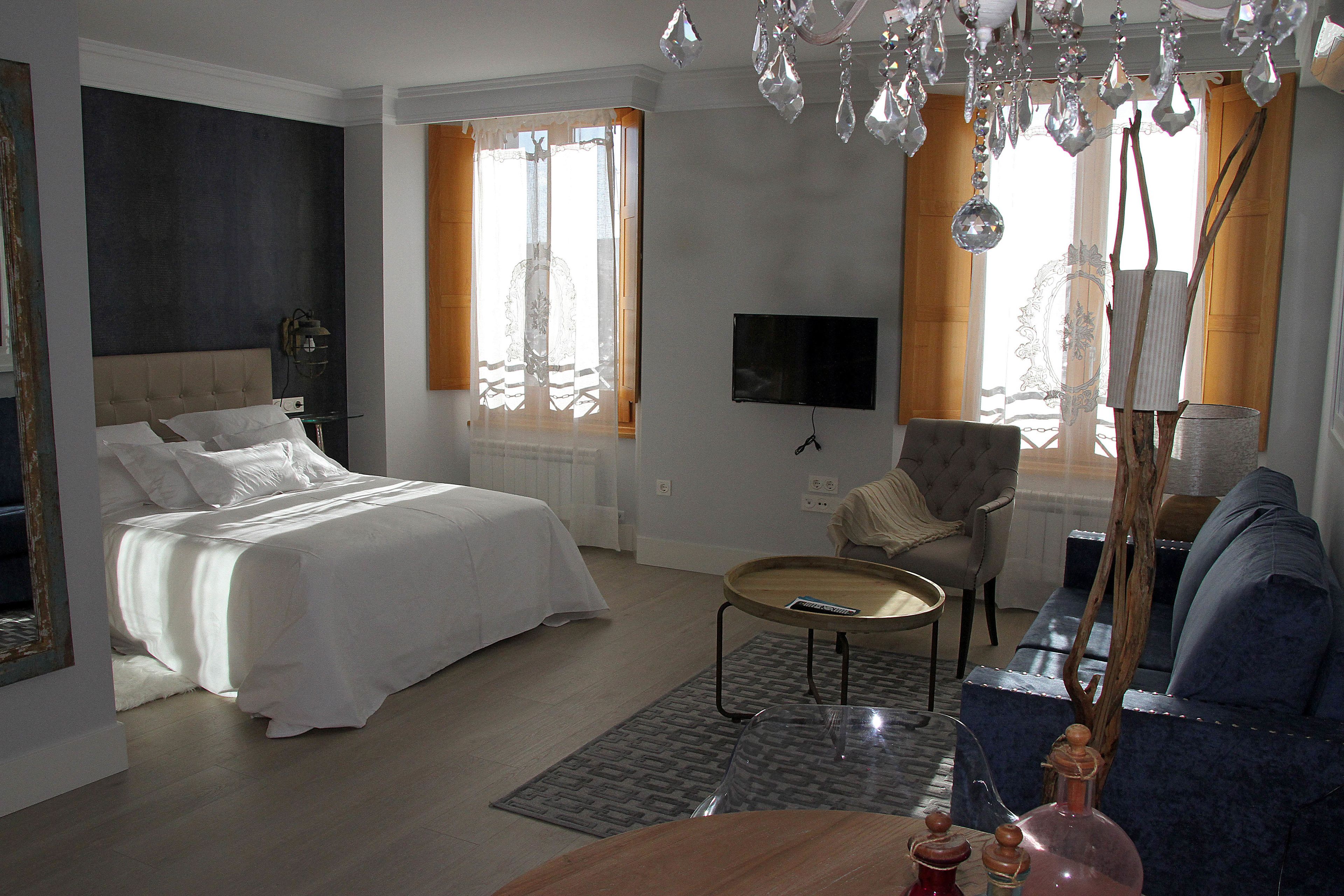 A hotel room with a bed, a sofa, a TV, and a chandelier.