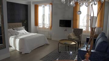 A hotel room with a bed, a sofa, a TV, and a chandelier.