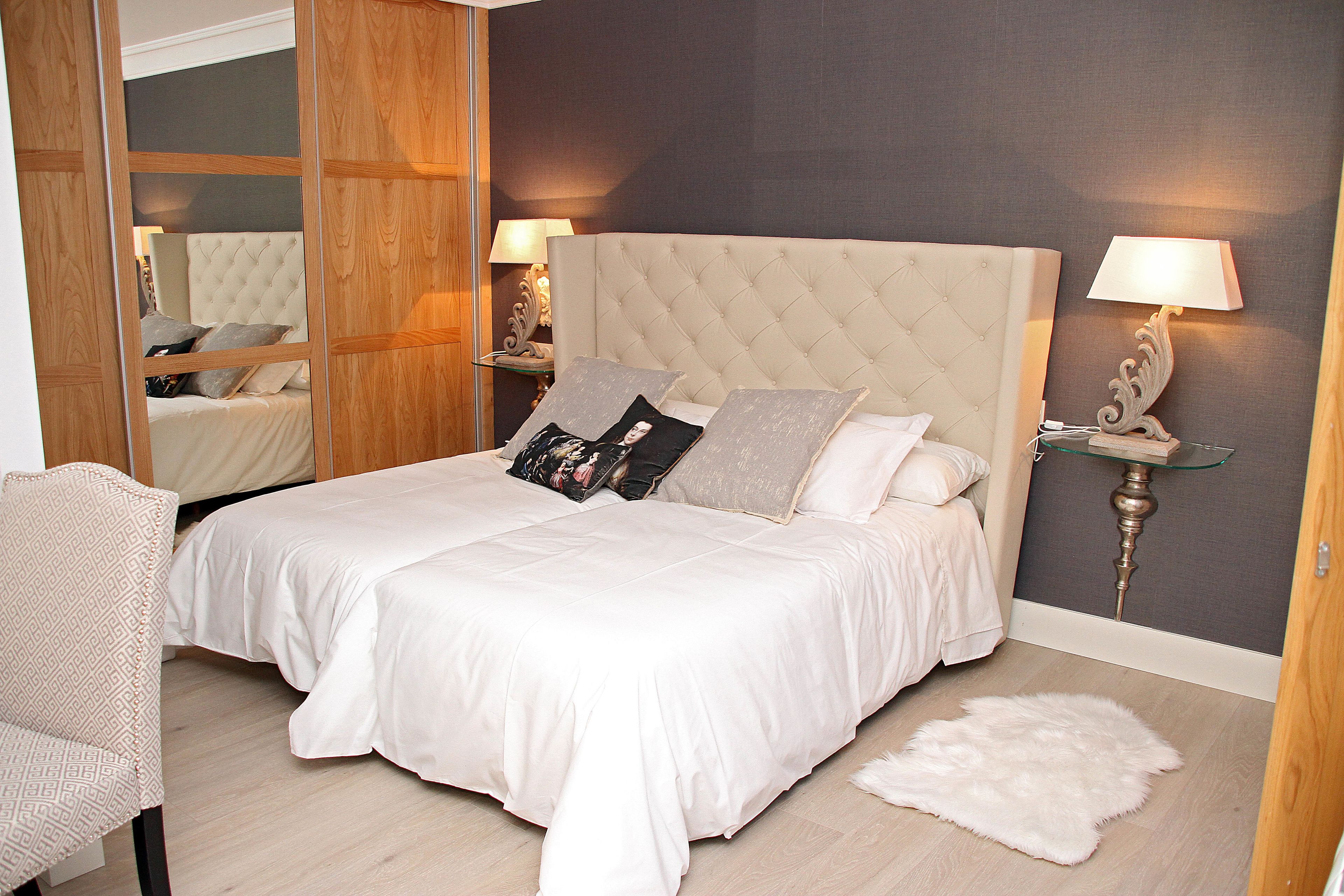 A bedroom with a large bed, two bedside tables with lamps, a chair, and a mirror.