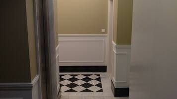 A hallway with a black and white checkered floor, a light-colored wall, and a ceiling with recessed lighting.