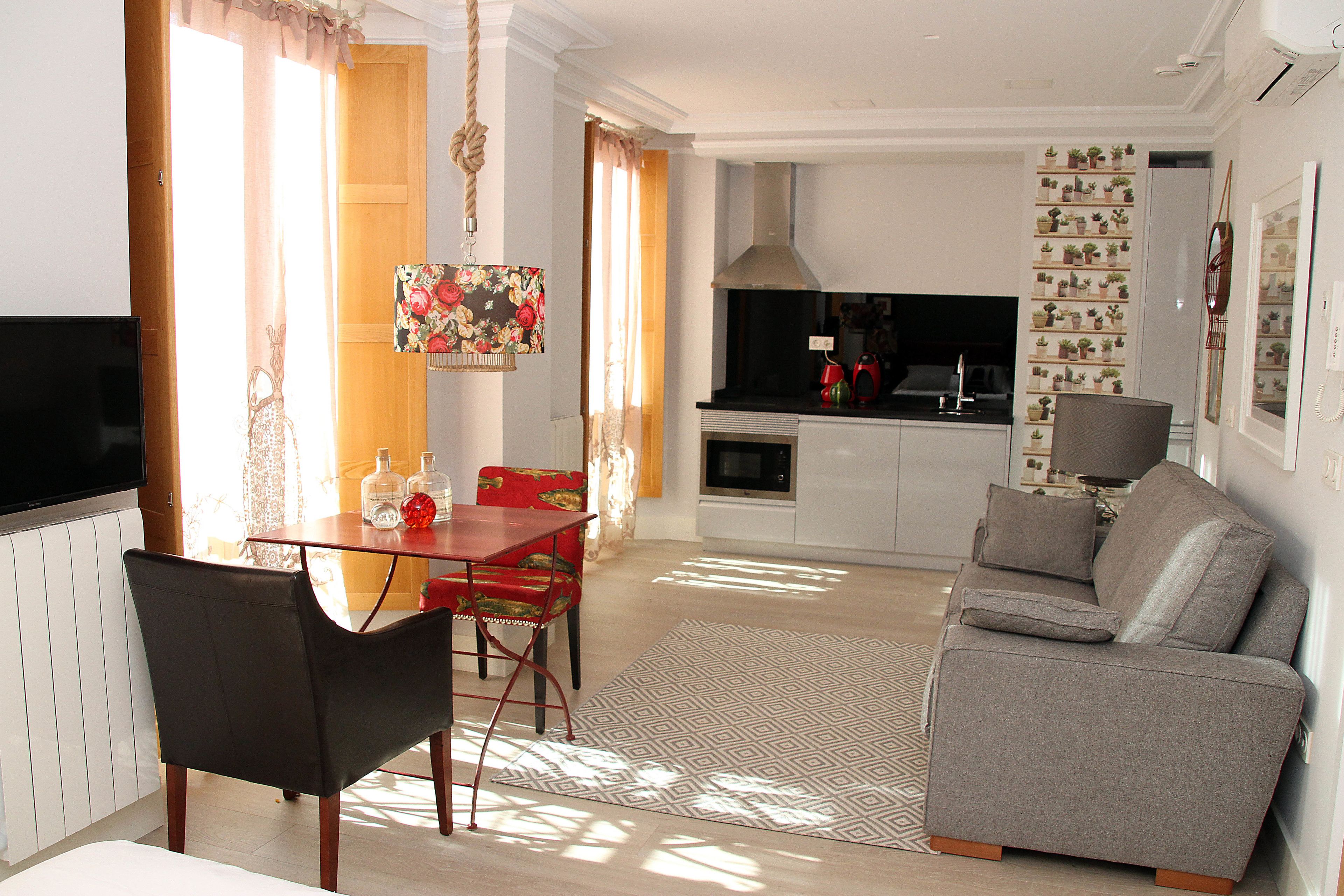 A modern living room with a grey sofa, a dining table with chairs, a flat-screen TV, and a kitchen area with a stove, oven, and microwave.