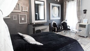 Une chambre à coucher avec un grand lit, deux fauteuils, une petite table, un miroir et une cheminée.