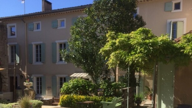 Une piscine avec une statue au centre, entourée de bâtiments dotés de volets et de verdure.