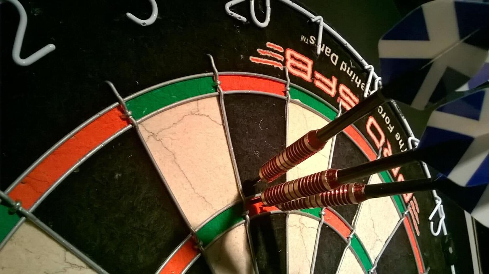 Eine Dartscheibe mit drei Dartpfeilen in der Mitte, schwarzem Hintergrund und den Zahlen 20 und 3.