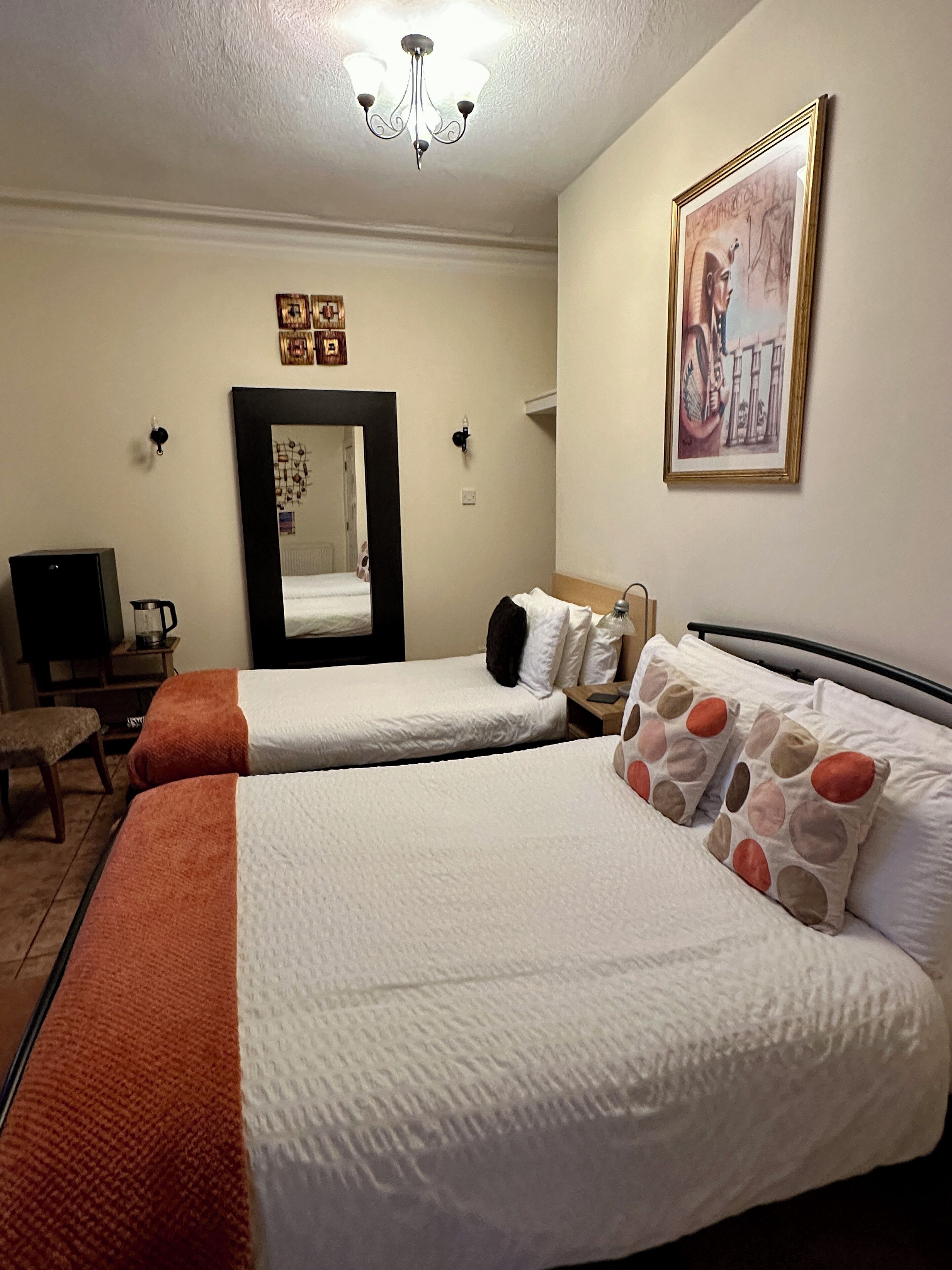 Une chambre d’hôtel avec deux lits, un grand miroir, un tableau et un lustre.