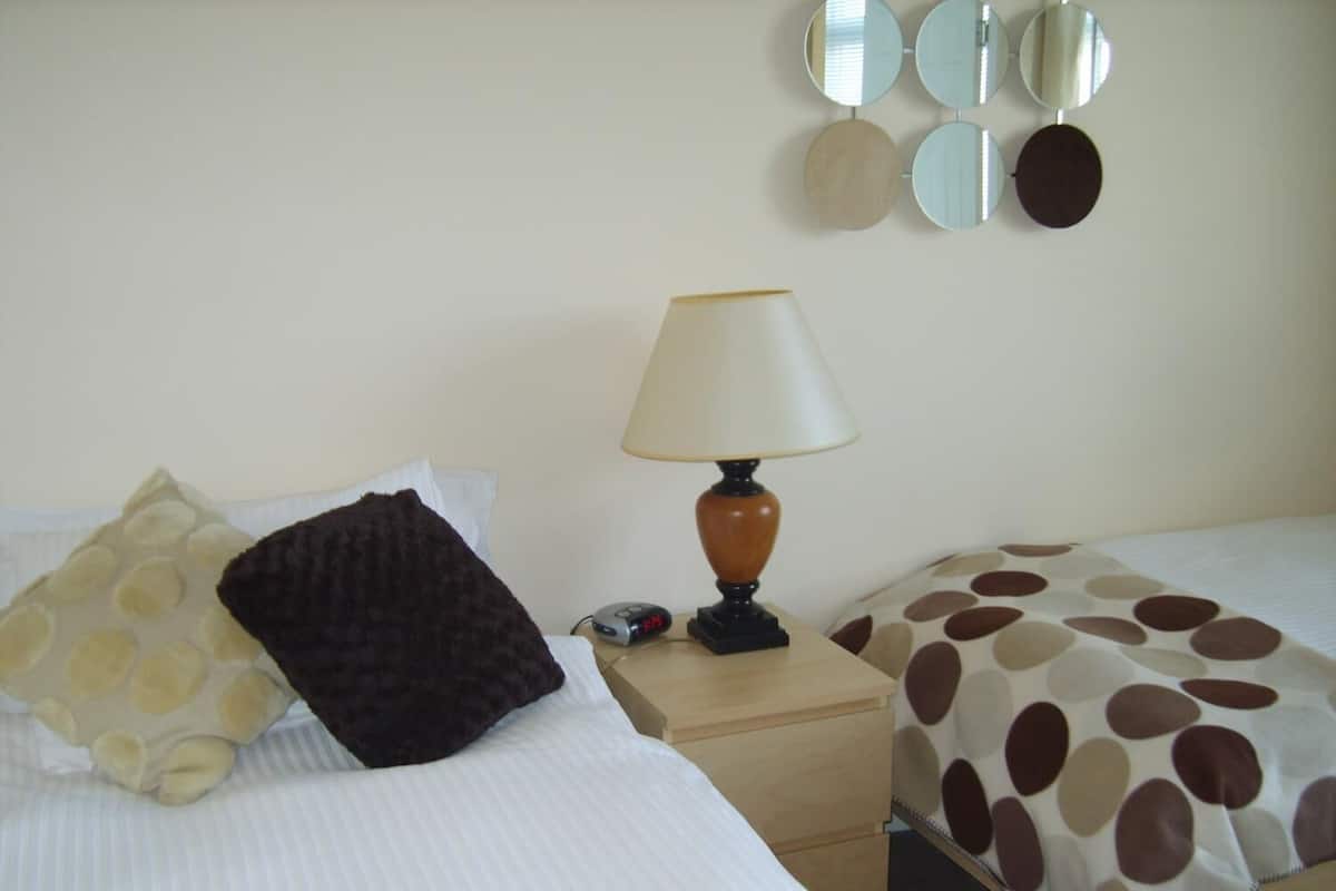 A hotel room with a bed, a bedside table with a lamp, a clock, and a wall with mirrors.