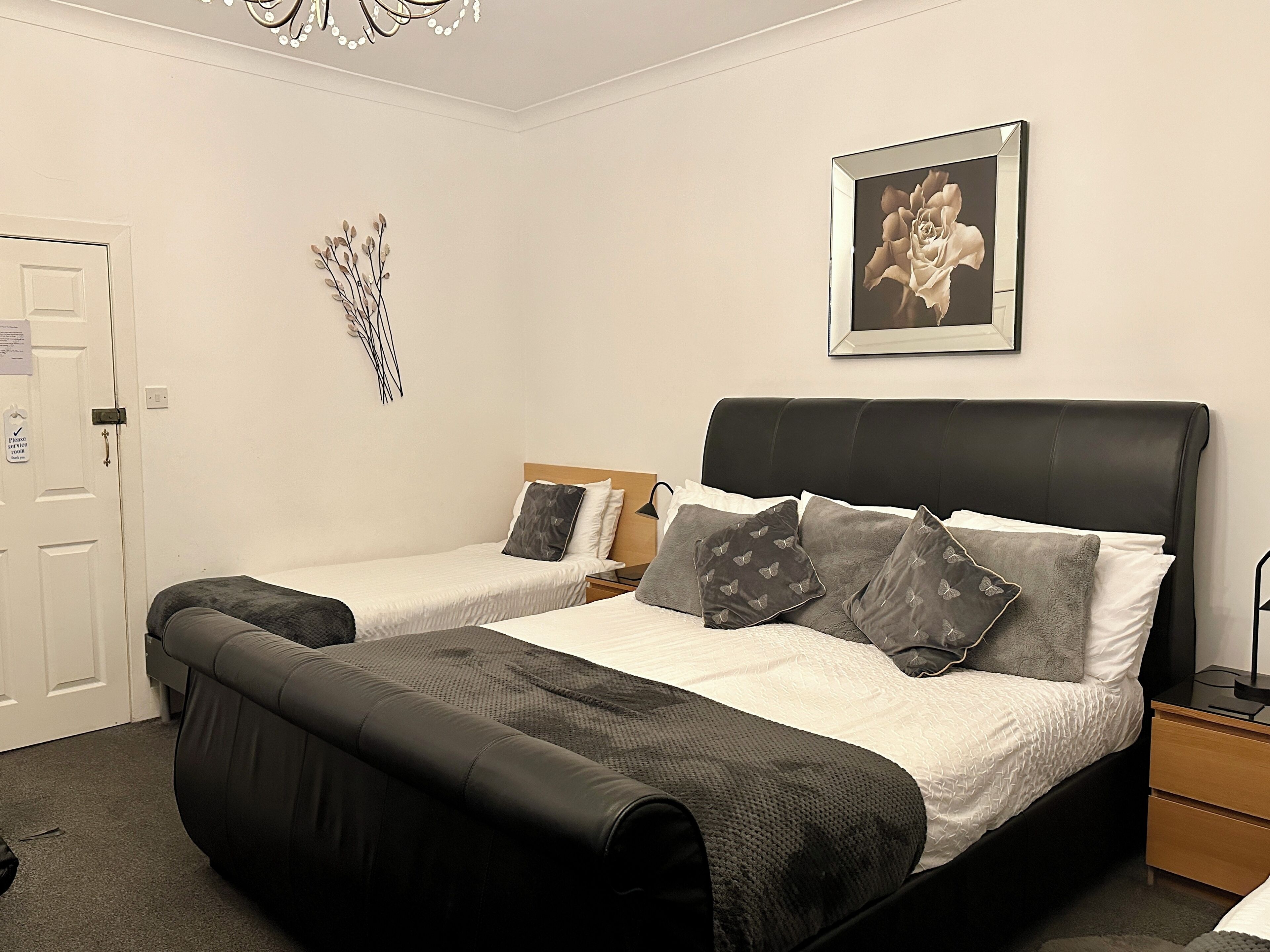 A double bed with a black headboard, two bedside tables, a nightstand, and a wall-mounted picture.