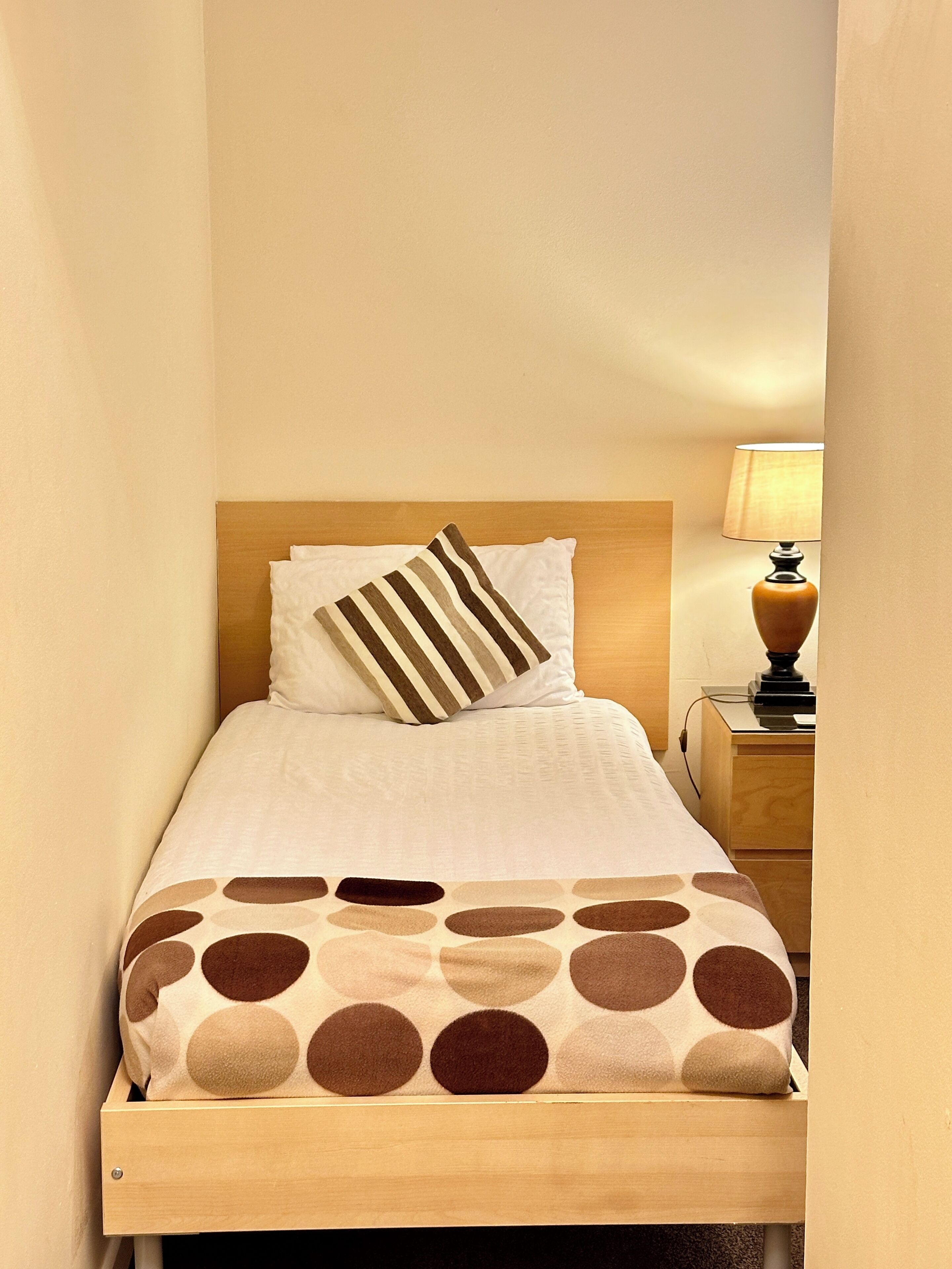 A neatly made bed with a striped pillow, a polka dot blanket, and a bedside lamp on a wooden nightstand.