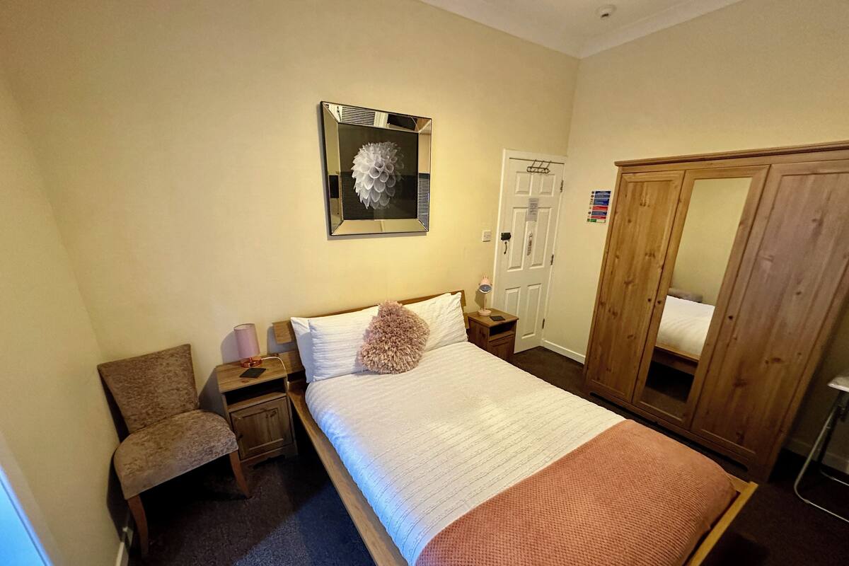 A bedroom with a bed, a chair, a wardrobe, a mirror, and a door.