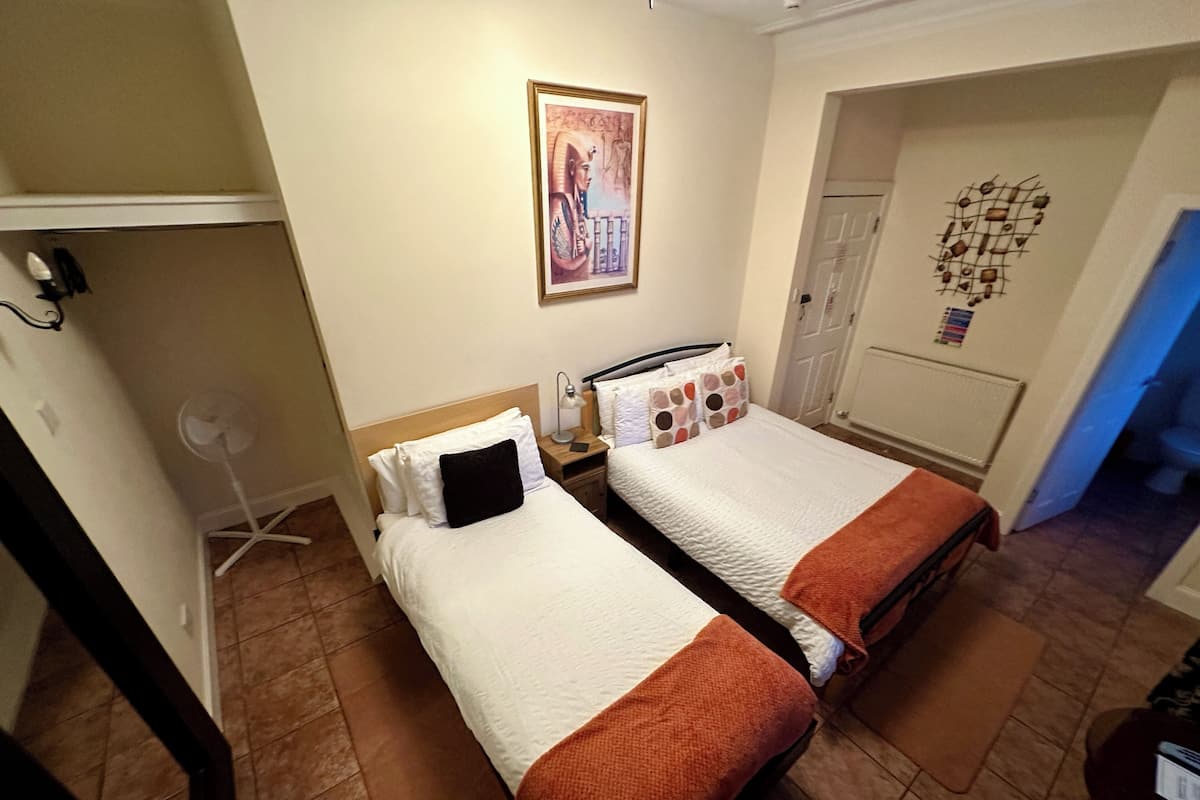 A hotel room with two beds, a fan, a nightstand, a poster on the wall, and a door leading to another room.