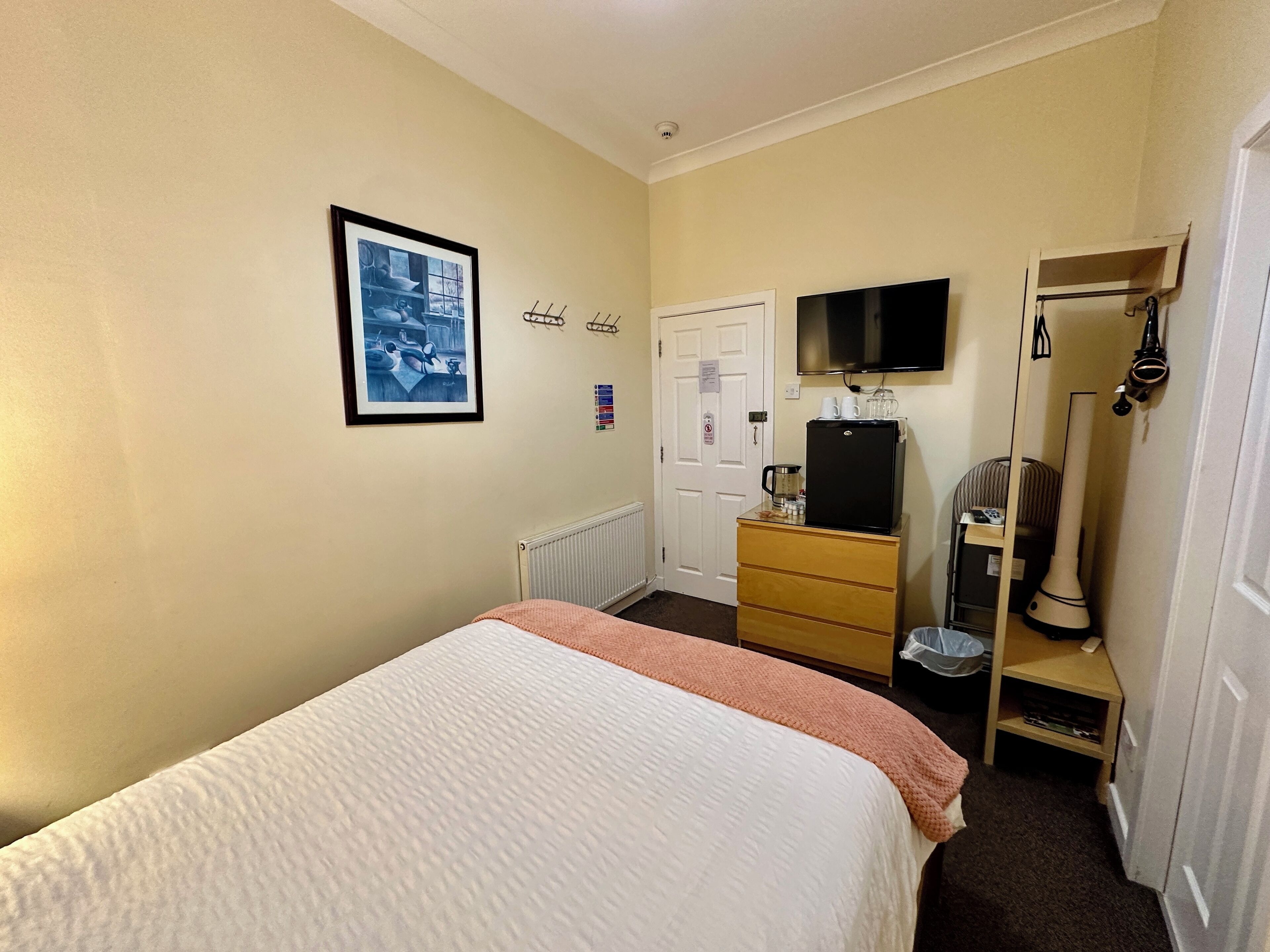 Una camera d'albergo con un letto, una cassettiera, una televisione e un termosifone.