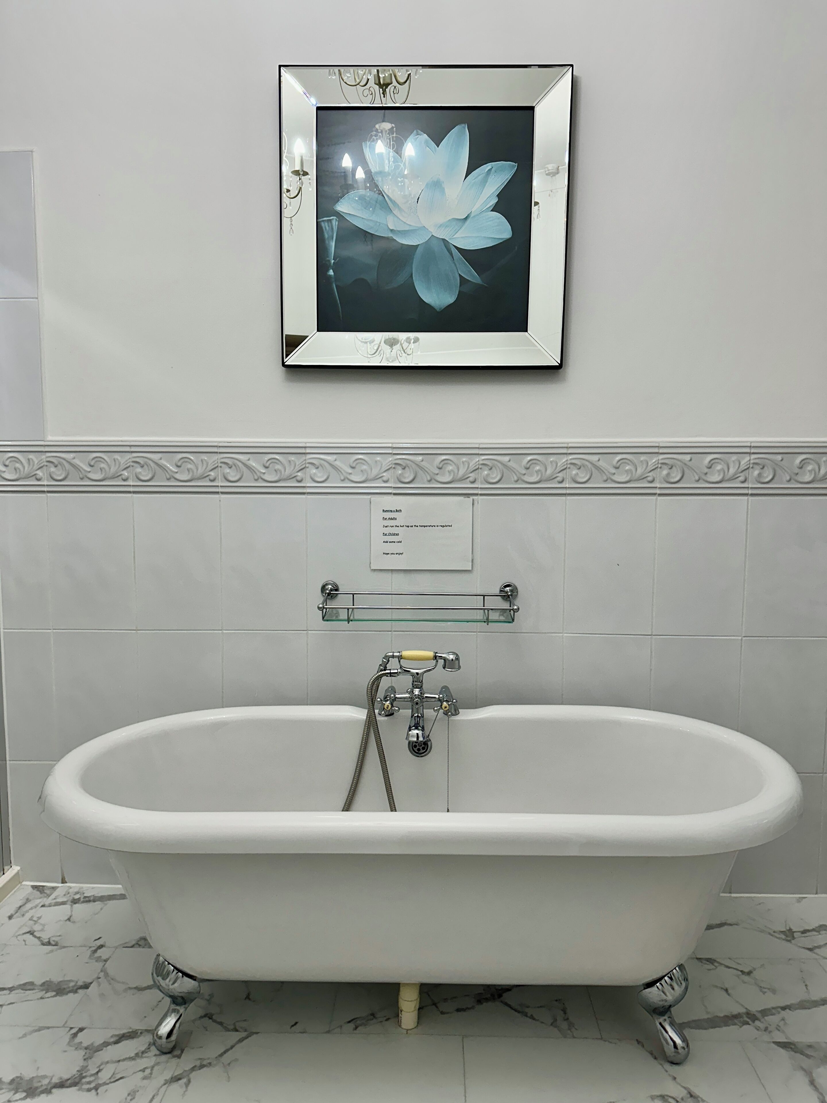Une salle de bain avec une baignoire sur pieds, une œuvre d’art florale encadrée, un porte-serviettes et un panneau décoratif mural.