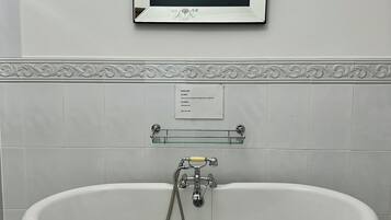 Une salle de bain avec une baignoire sur pieds, une œuvre d’art florale encadrée, un porte-serviettes et un panneau décoratif mural.