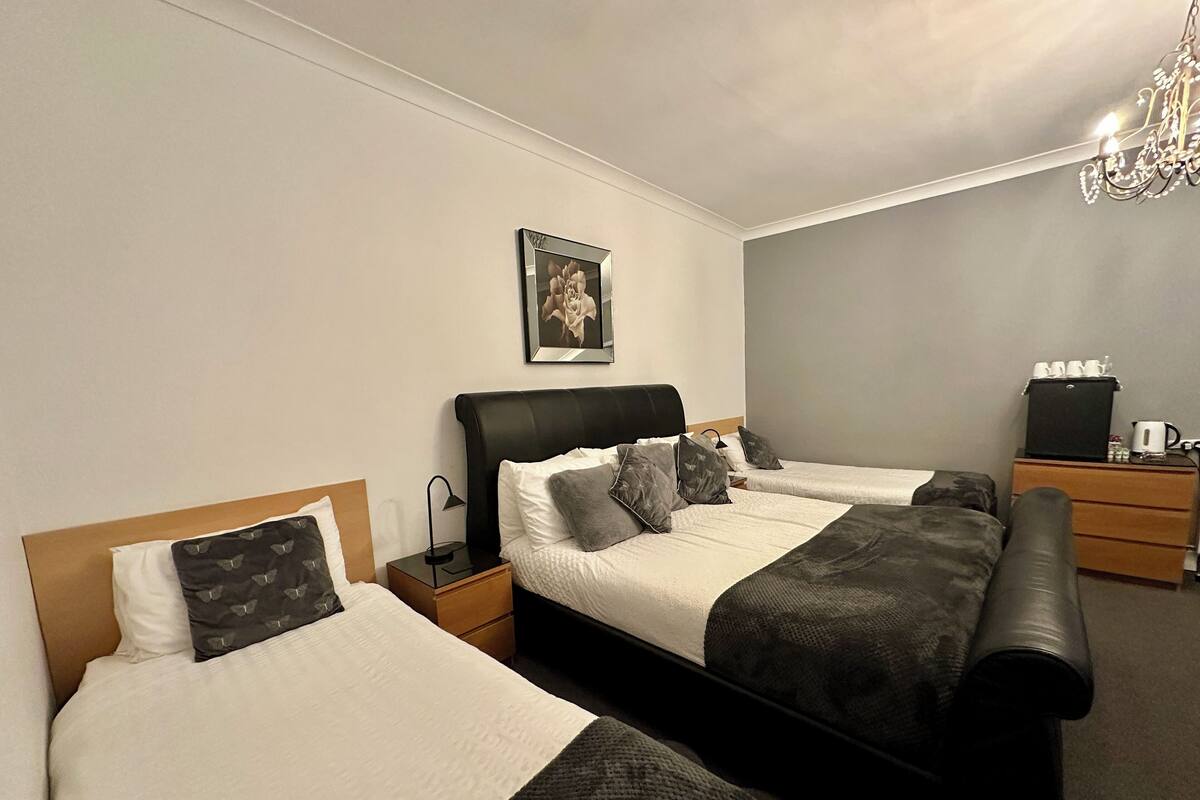 A hotel room with two beds, a nightstand with a lamp, a dresser, a coffee maker, and a framed picture on the wall.