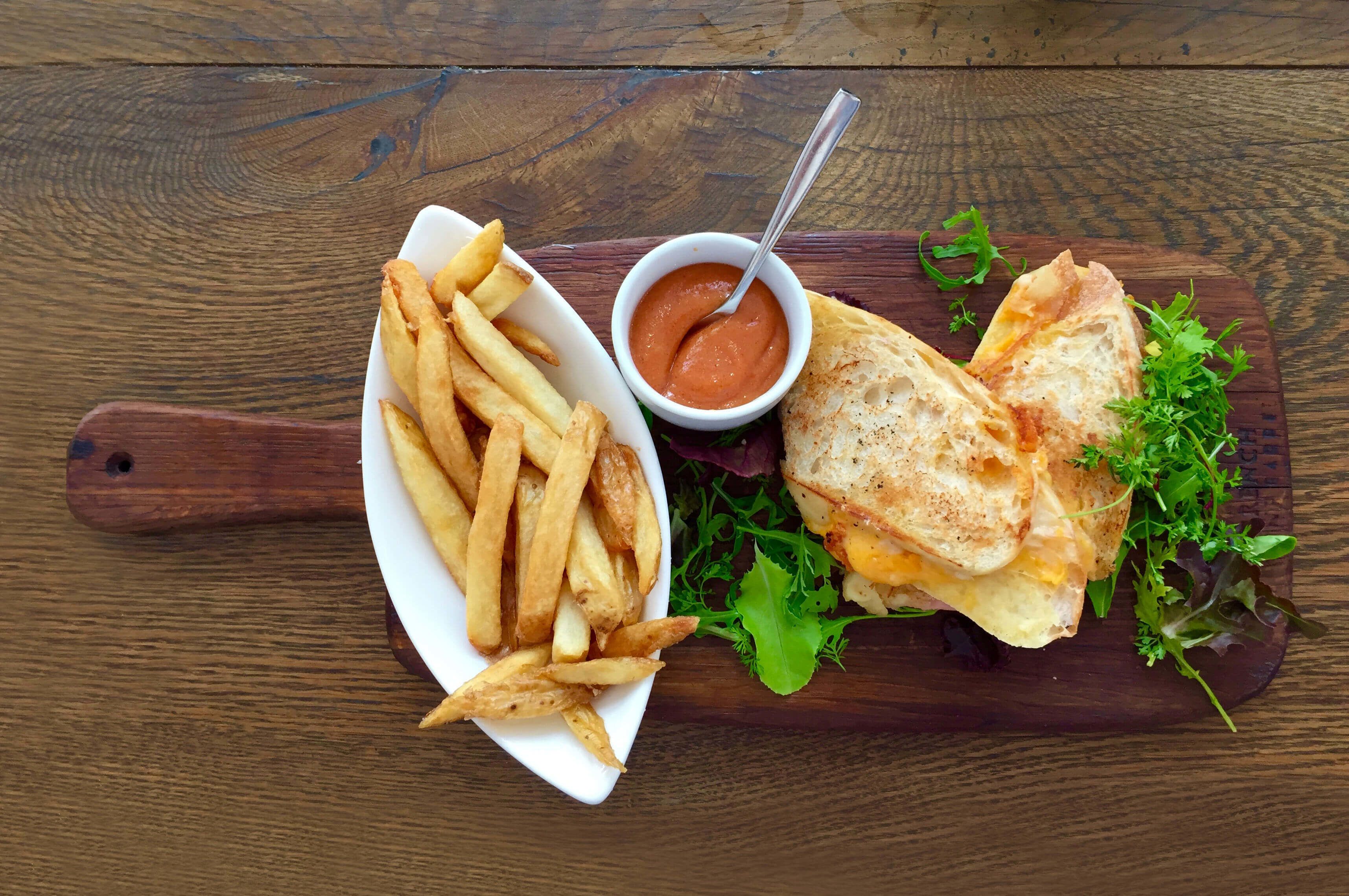 Comida que incluye un sándwich, papas fritas y una salsa para mojar sobre una tabla de madera.