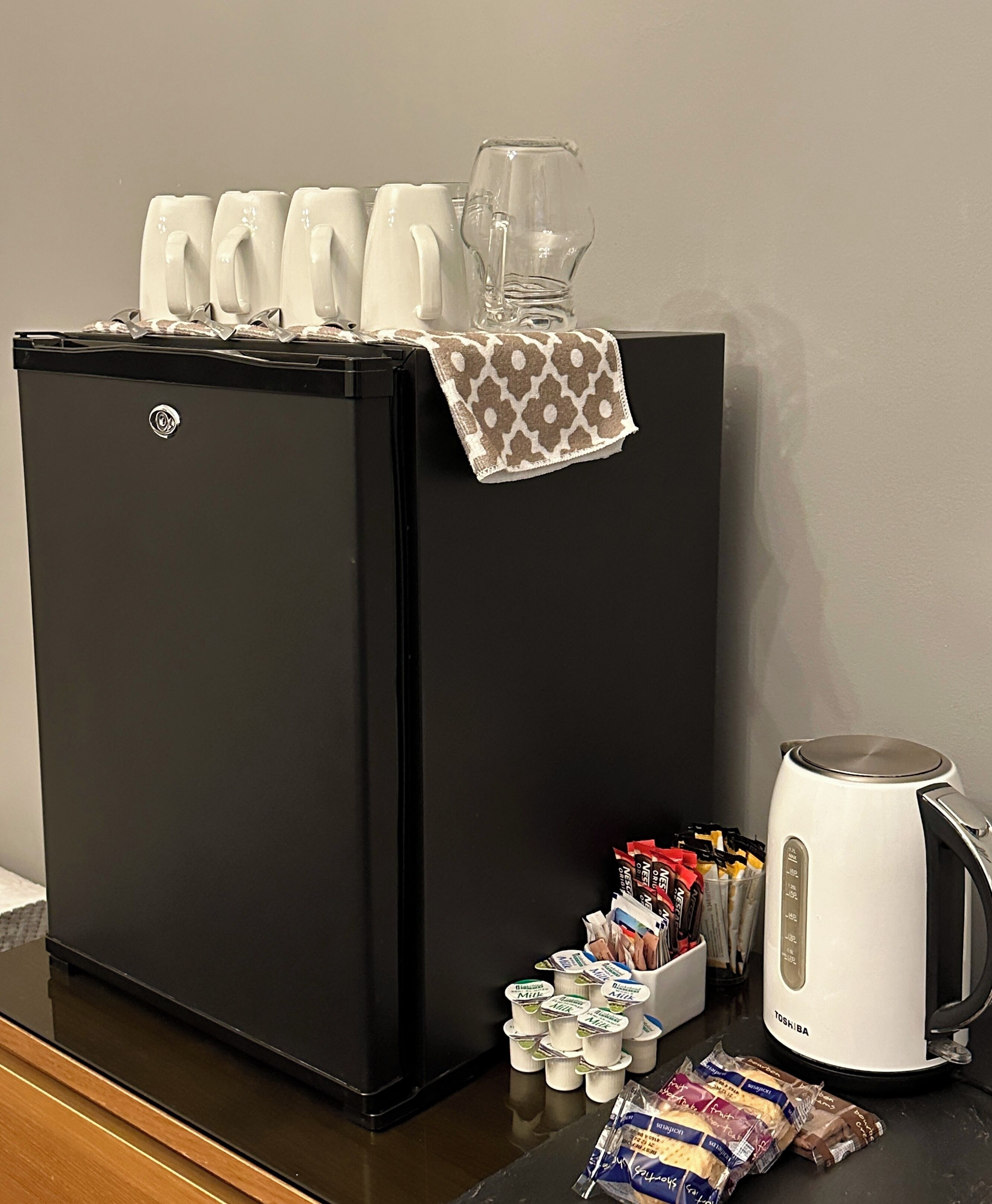 A black refrigerator with a glass pitcher and a white kettle on the counter.