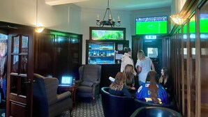 A bar area with seating, a television screen, and a bar counter with various bottles. - The Elbow Room (Kirkcaldy)