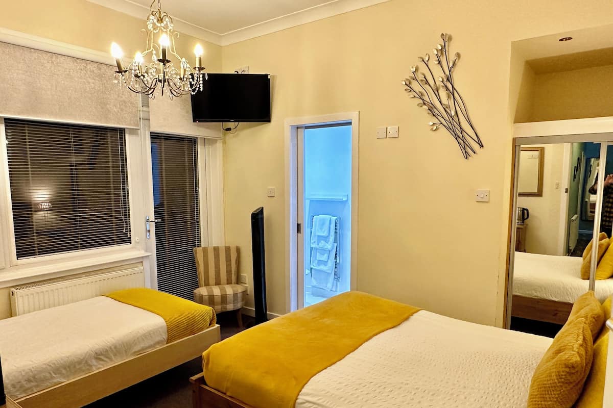 A hotel room with two single beds, a chandelier, a TV, and a view of the outside balcony.