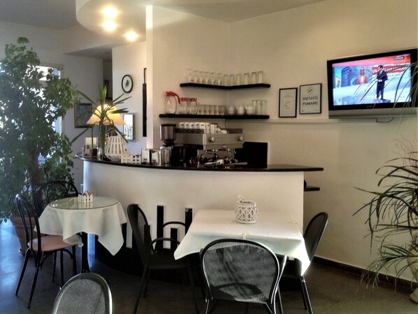Een café met een toonbank, stoelen, tafels, een televisie en planten.