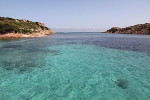 Een kustlandschap met helder turquoise water, rotsachtige kliffen en schaarse begroeiing.