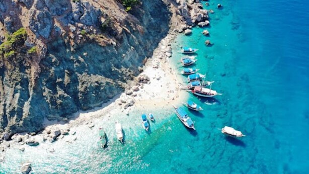 An aerial view of a coastal area with boats docked along a rocky shoreline. - 7 Green Adrasan (Kumluca)