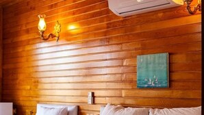 A hotel room with wooden paneling, a bed with white linens, an air conditioning unit, and wall-mounted sconces. - 7 Green Adrasan (Kumluca)