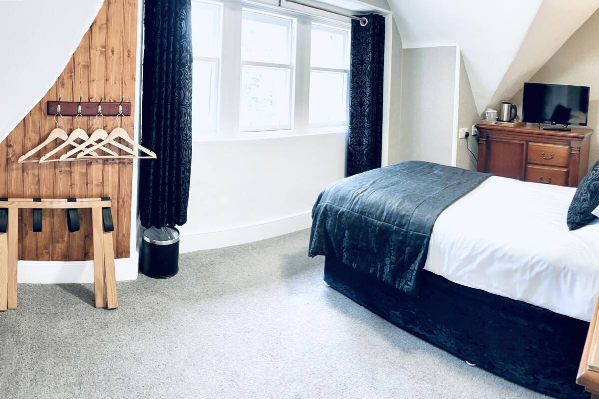 A bedroom with a bed, a dresser, a TV, and a wooden chair.