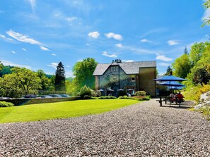 A stone building with a large lawn, a gravel path, and a picnic area with umbrellas.