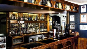A bar area with shelves stocked with various liquor bottles, a tap, and a counter with a cash register. - Invergarry Hotel (Invergarry)