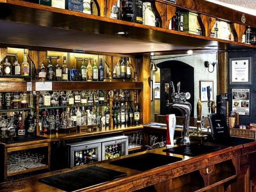 Zona de bar con estantes llenos de botellas de licores, una grifería y un mostrador con una caja registradora.