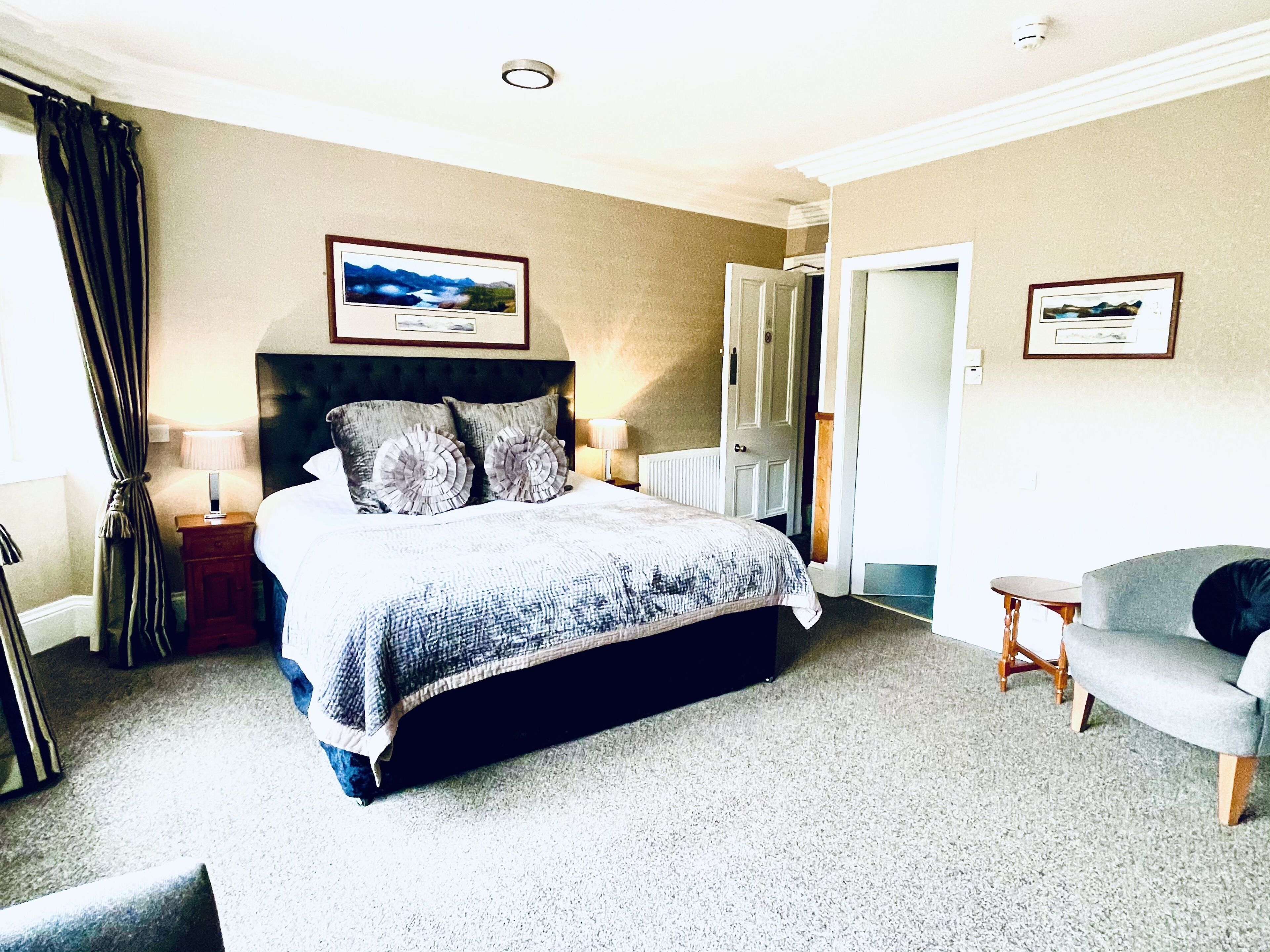 Une chambre à coucher avec un lit, deux lampes de chevet, une chaise, une porte et deux tableaux encadrés accrochés au mur.