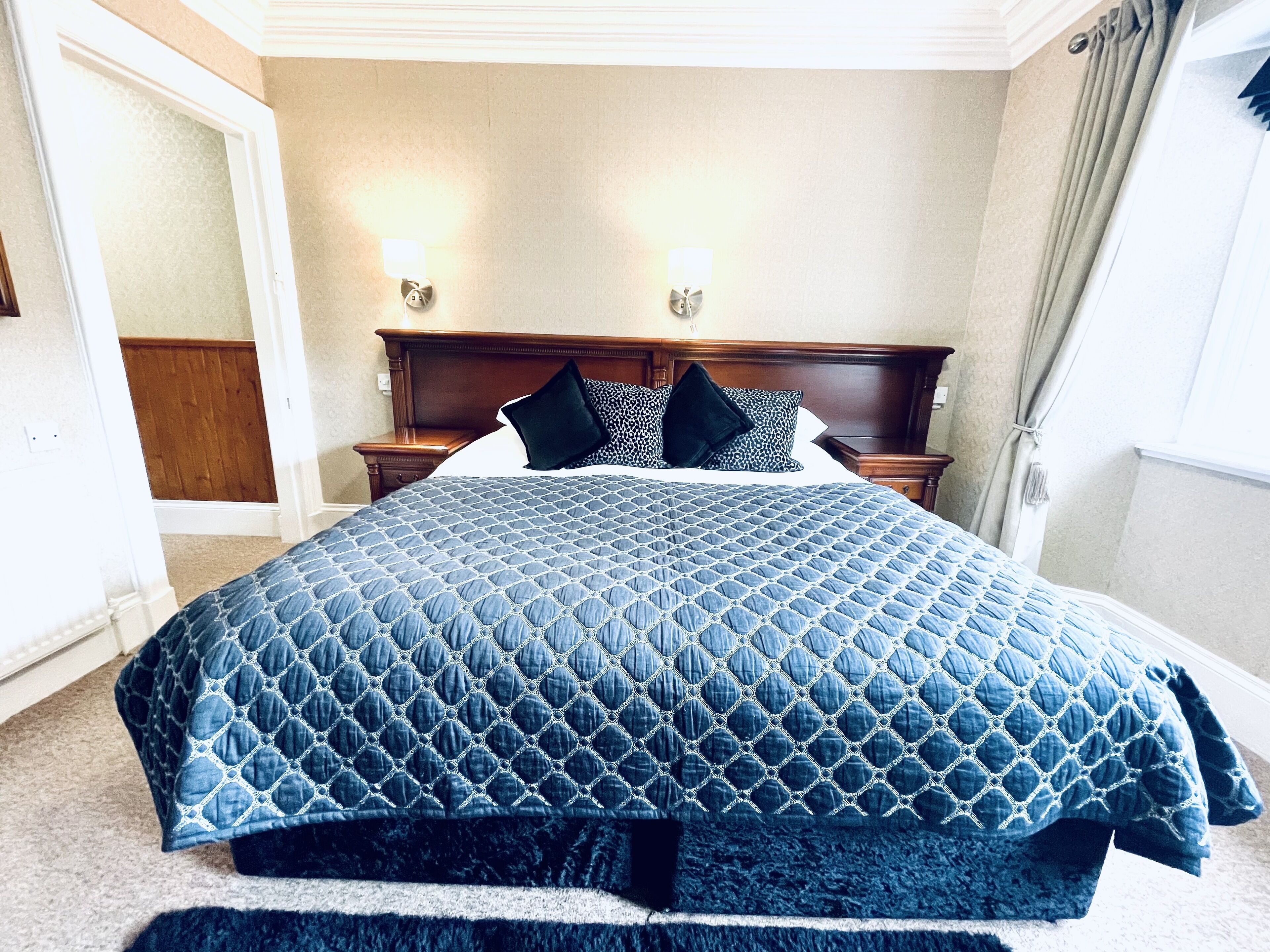 A large bed with a quilted blue cover, two bedside tables with lamps, and a wooden headboard.