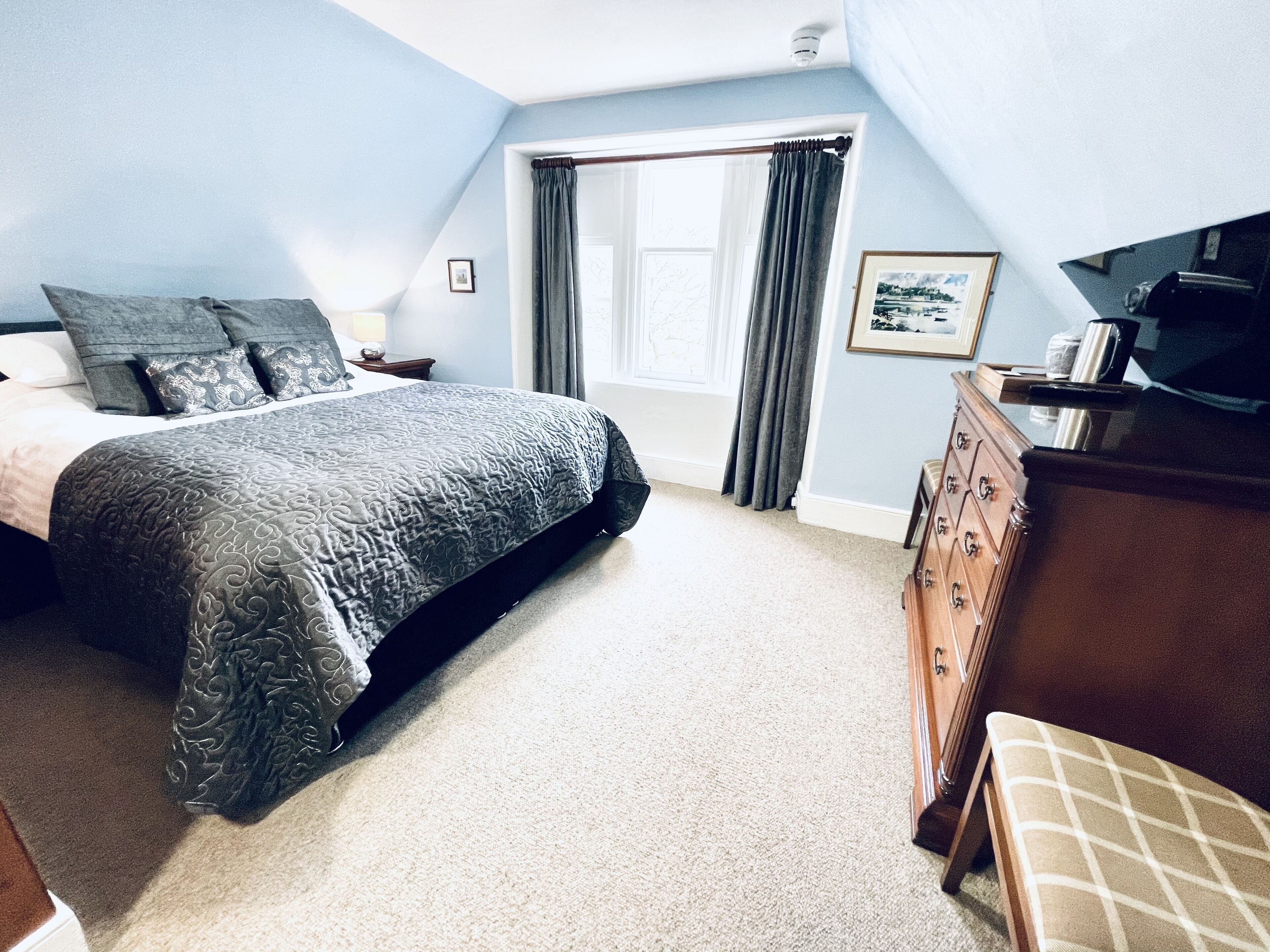 A bedroom with a large bed, a dresser, a television, and a window with curtains.